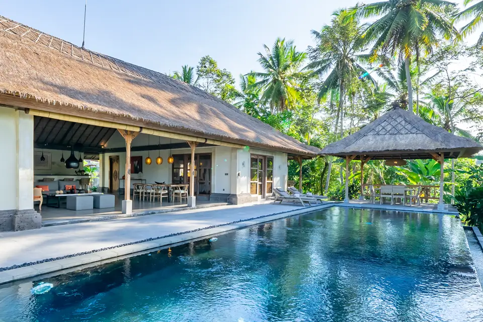 A pool and open-air living space surrounded by palms at Villa Jae in Bali